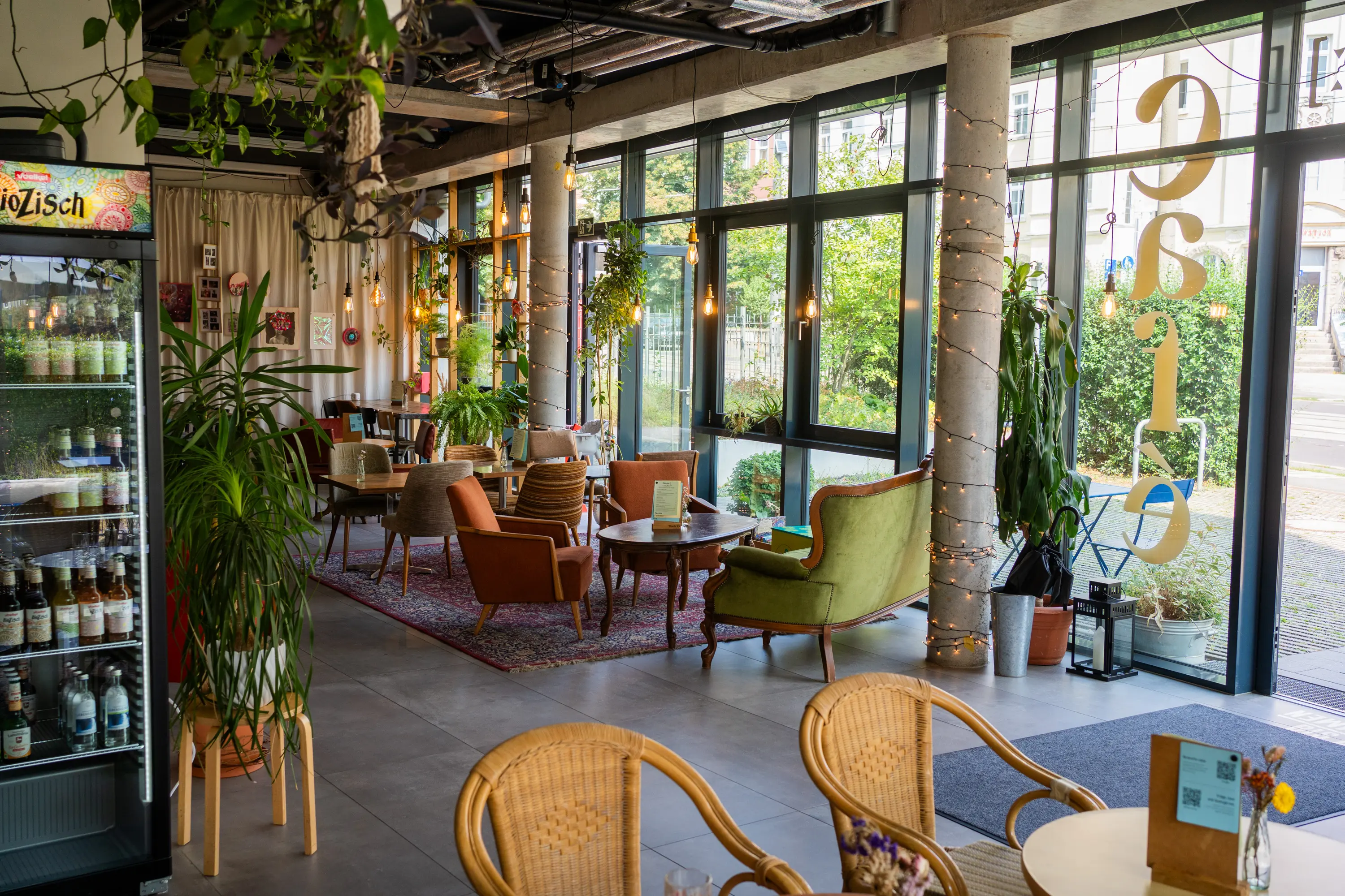 Lichtdurchflutetes kate Café in Erfurt mit Vintage-Sesseln, Pflanzen und großer Fensterfront – Veranstaltungsraum zum Mieten